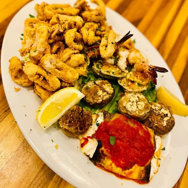 A large platter of fried calamari, shrimp, clams, stuffed mushrooms, and baked eggplant with marinara sauce.