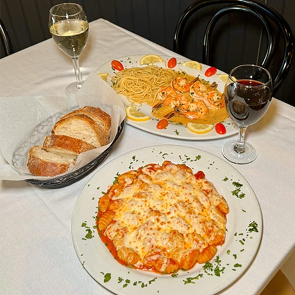 Table with Spaghettini's gnocchi, shrimp scampi, bread, and glasses of white and red wine.