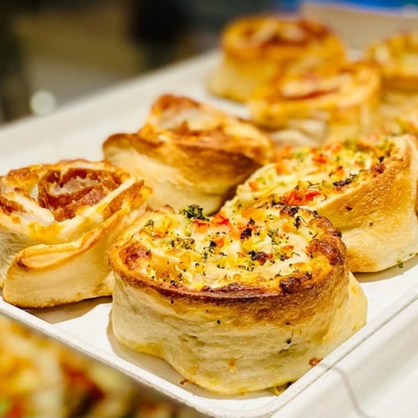 Close-up of several golden-brown Italian pizza pinwheels with various toppings on a white tray.