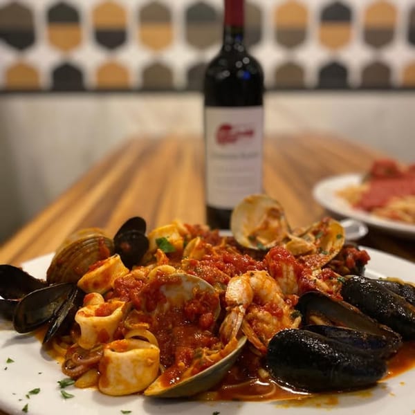 Seafood pasta with mussels, clams, calamari, and shrimp in red sauce, with a wine bottle.