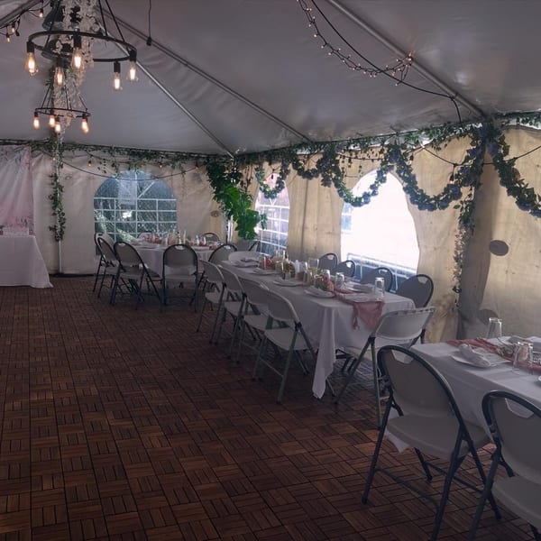 A large white event tent with long tables set for dining, decorated with string lights and greenery.