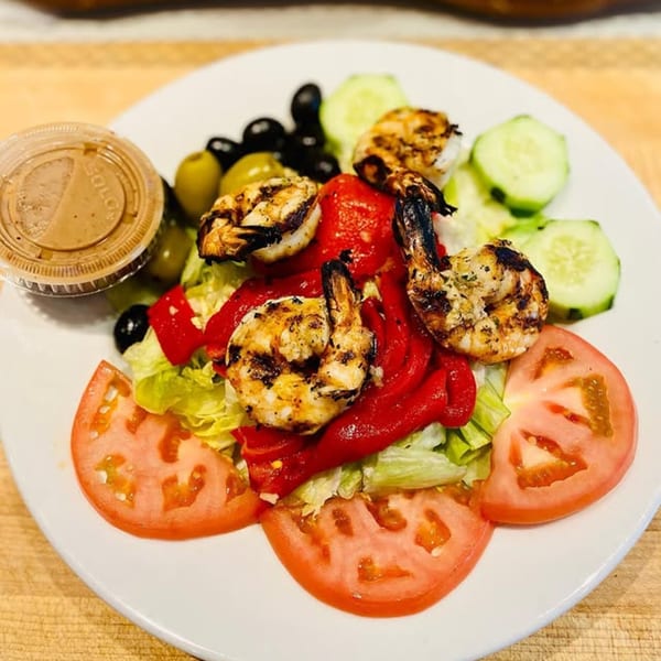 Grilled shrimp salad with lettuce, tomatoes, cucumbers, olives, roasted red peppers, and dressing.