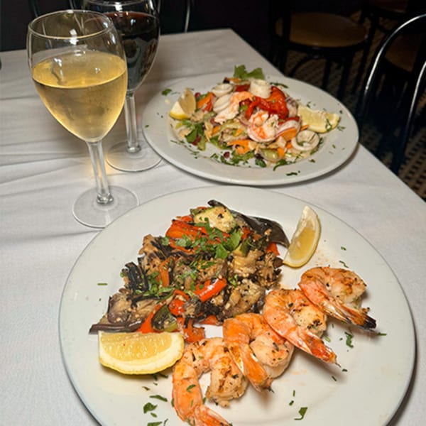 Two plates of Italian seafood and vegetable dishes, with glasses of white and red wine.