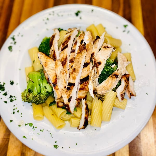 Grilled chicken and broccoli served over rigatoni pasta, garnished with fresh parsley.