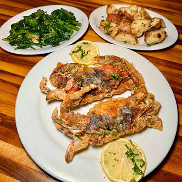 Fried soft-shell crabs with lemon, roasted potatoes, and sautéed greens on a wooden table.