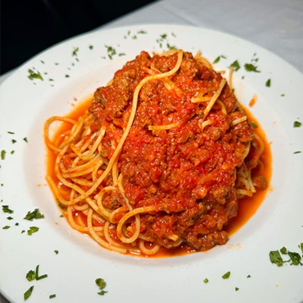 A white plate of Spaghettini with rich red Bolognese sauce and fresh parsley garnish.