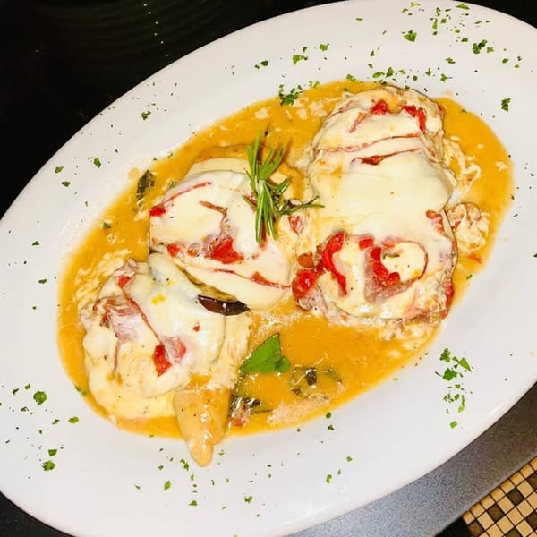 Italian chicken dish with melted cheese, red peppers, and rosemary in a rich sauce.
