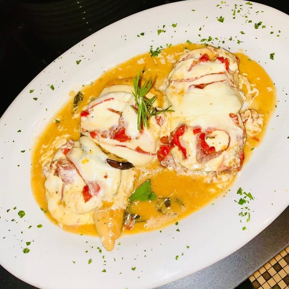 Italian chicken dish with melted cheese, red peppers, and rosemary in a rich sauce.