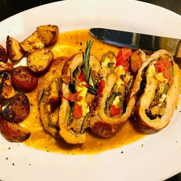 Italian chicken roulade stuffed with vegetables and cheese, served with roasted potatoes and a knife.