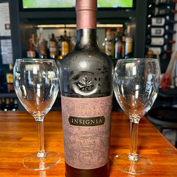 A bottle of Joseph Phelps Insignia wine and two empty wine glasses on a wooden bar.