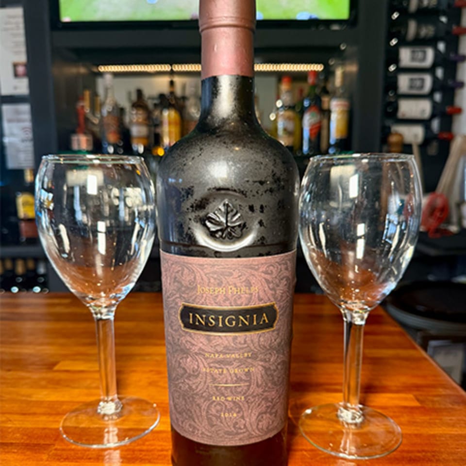 A bottle of Joseph Phelps Insignia wine and two empty wine glasses on a wooden bar.