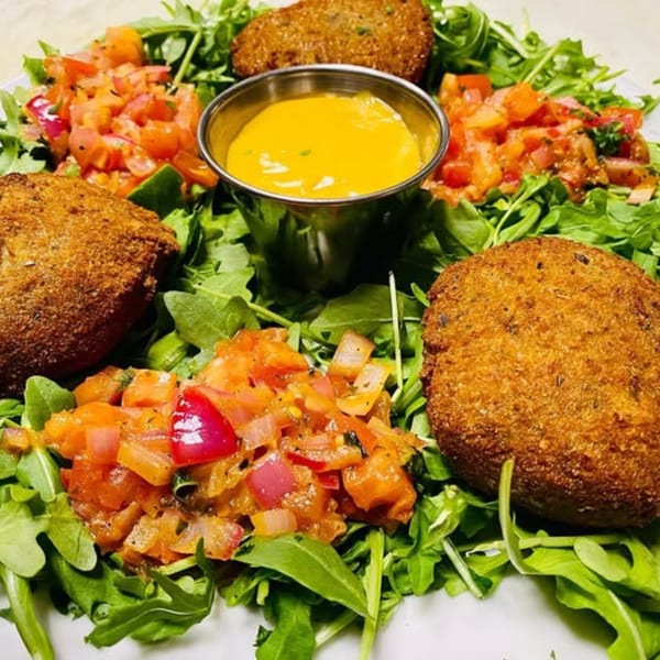 Fried arancini balls with fresh arugula, diced tomatoes, and a side of yellow sauce.