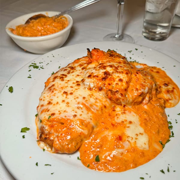 Chicken parmesan with melted cheese and red sauce, served with a side of pasta.