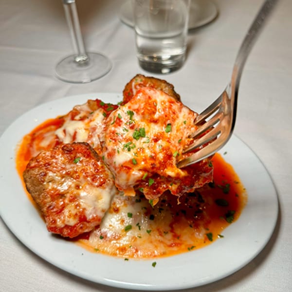A fork lifts a cheesy meatball from a plate of Spaghettini Pizza Trattoria's meatballs in red sauce.