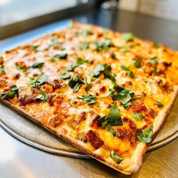 Square Spaghettini Pizza with melted cheese, meat, and fresh basil on a metal tray.