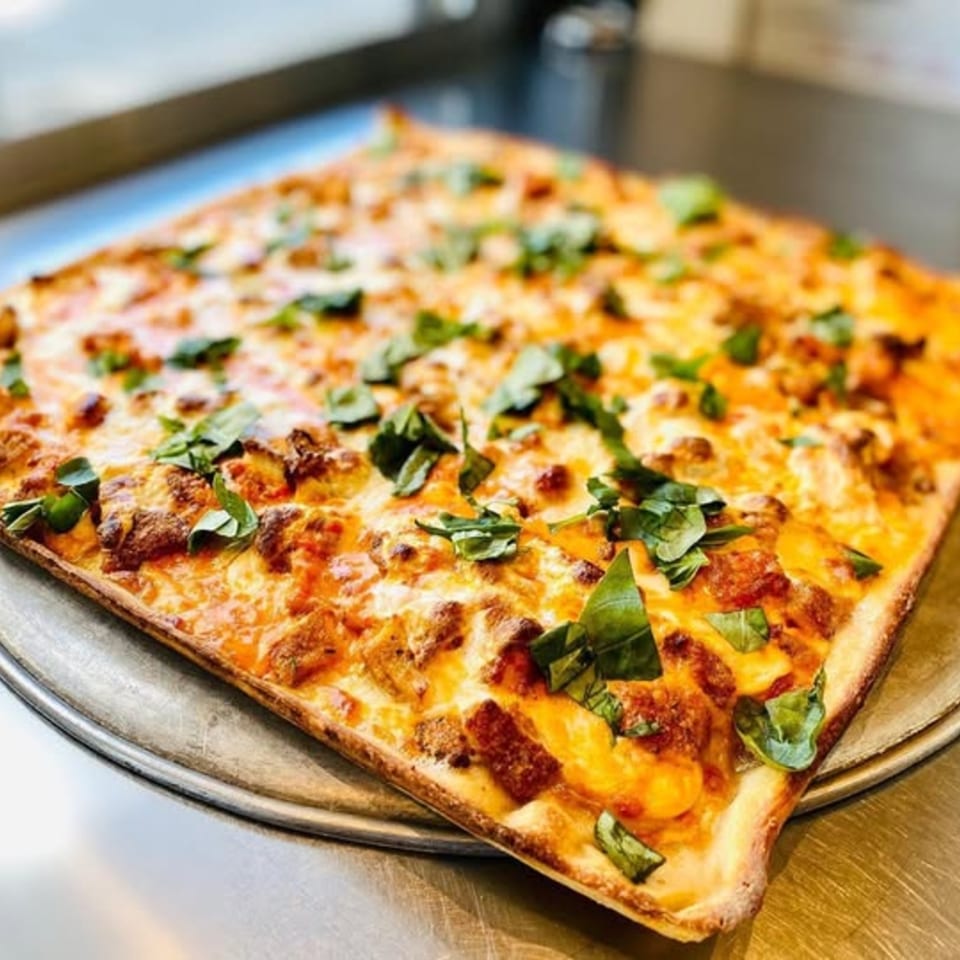 Square Spaghettini Pizza with melted cheese, meat, and fresh basil on a metal tray.