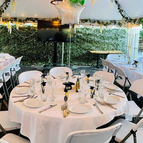 Outdoor tented dining area with white tables set for a graduation party at Spaghettini Pizza Trattoria.