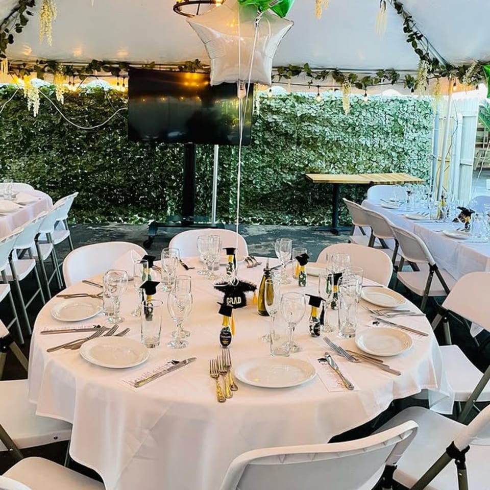 Outdoor tented dining area with white tables set for a graduation party at Spaghettini Pizza Trattoria.